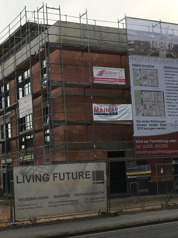 Ecke eines Wohnungsneubaus aus Ziegel, über vier Geschosse eingerüstet, mit Bauschildern an der Gerüstlage