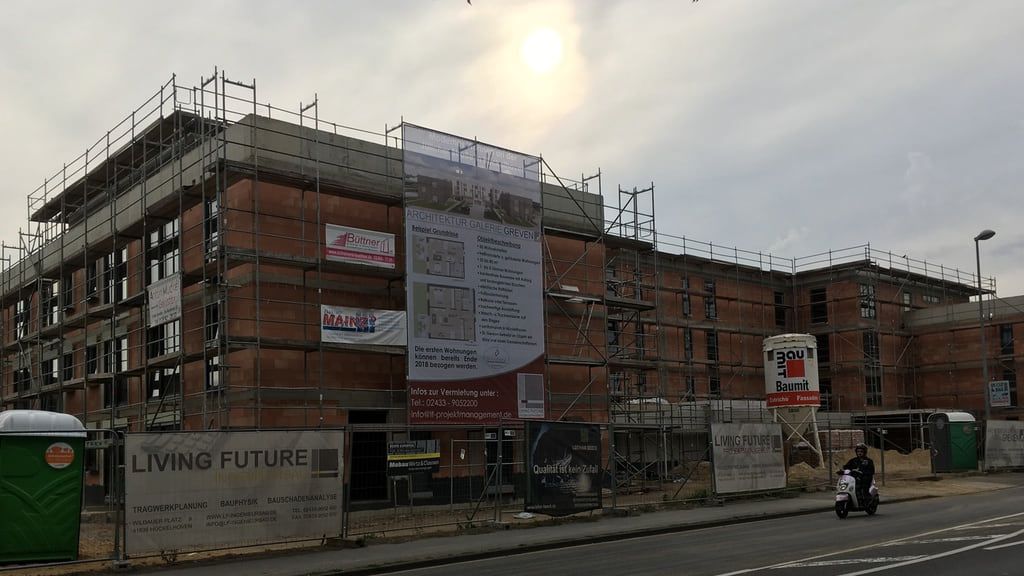 Blick von der gegenüberliegenden Straßenseite auf den eingerüsteten Wohnungsneubau in voller Länge