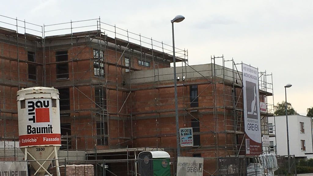 Baustelle hinter dem Bauzaun, Materialsilo und Sandschüttung vor dem eingerüsteten Gebäude